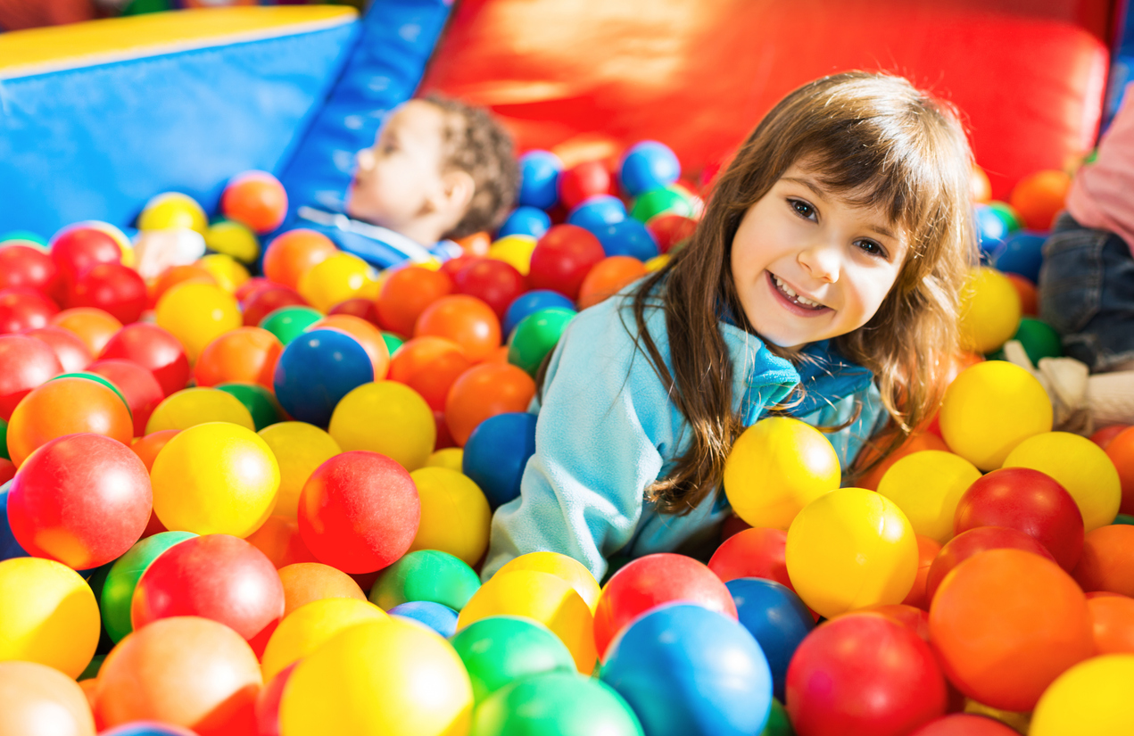 Children playing in the ball pool. Focus is on the girl in the foreground who is looking at the camera.